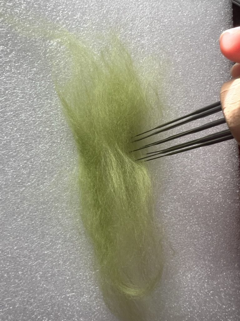 Artist using  needle felting tool to create a layer of green wool for needle felting 