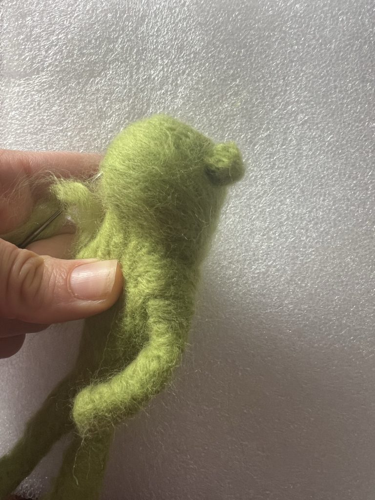 Artist needle felting a green frog doll 