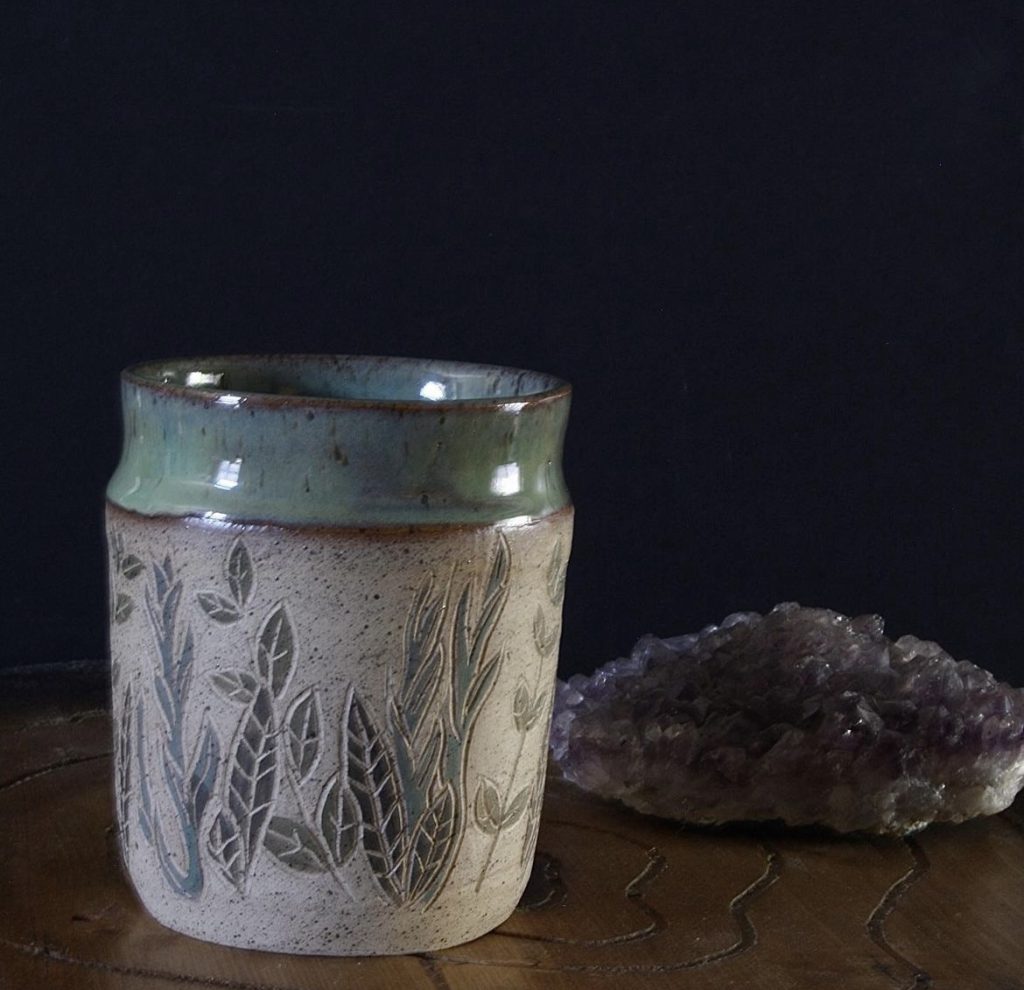 Ceramic cup with carved vines and leaves on it. Interior and rim are teal glaze