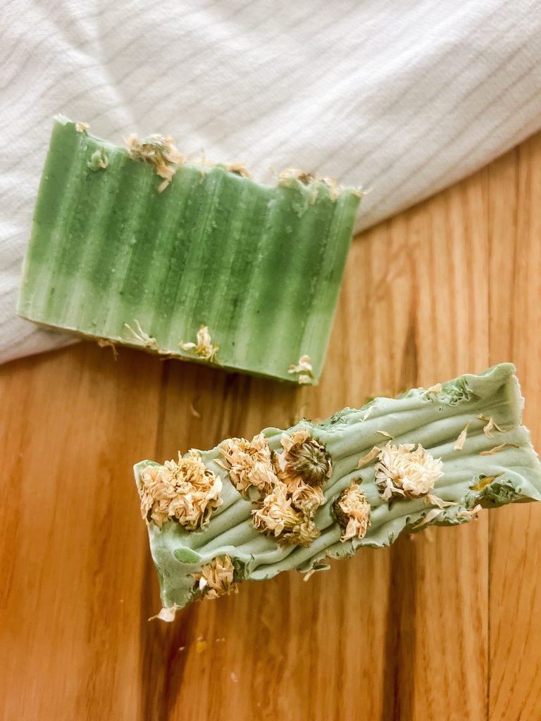 Handmade cold process soap on a wooden table with a white tea towel. Green aloe Vera and white lily handmade soap with dried flowers on top.