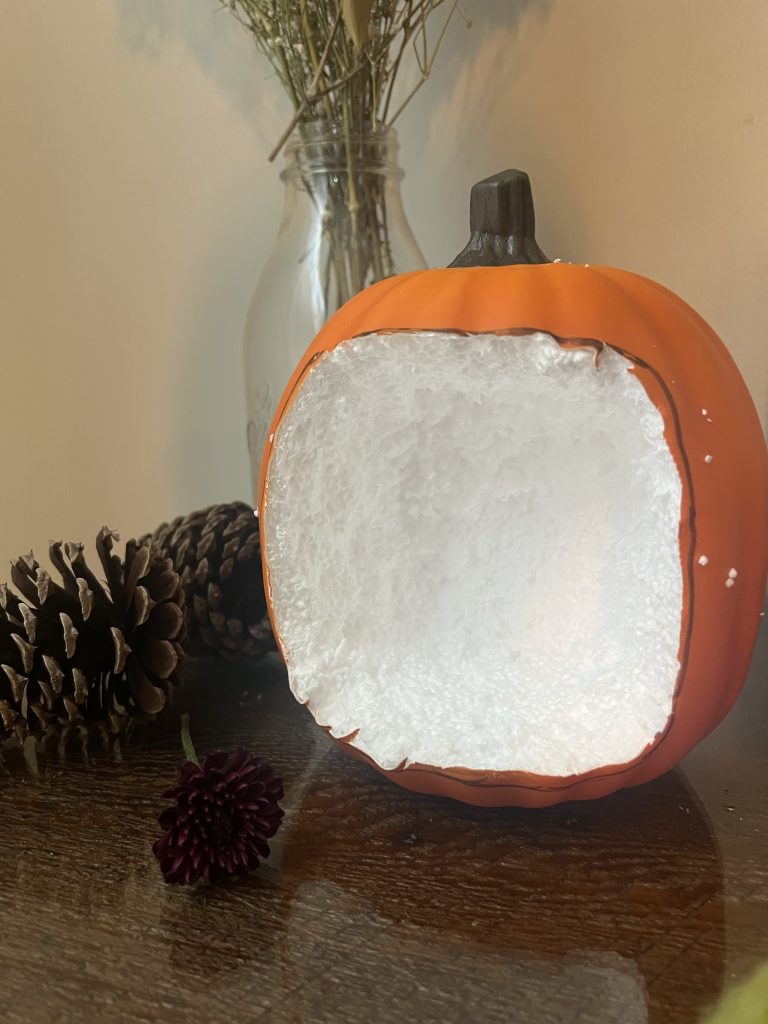 Photo of an orange hollowed out styrofoam pumpkin that is being made into a pumpkin fairy house 
