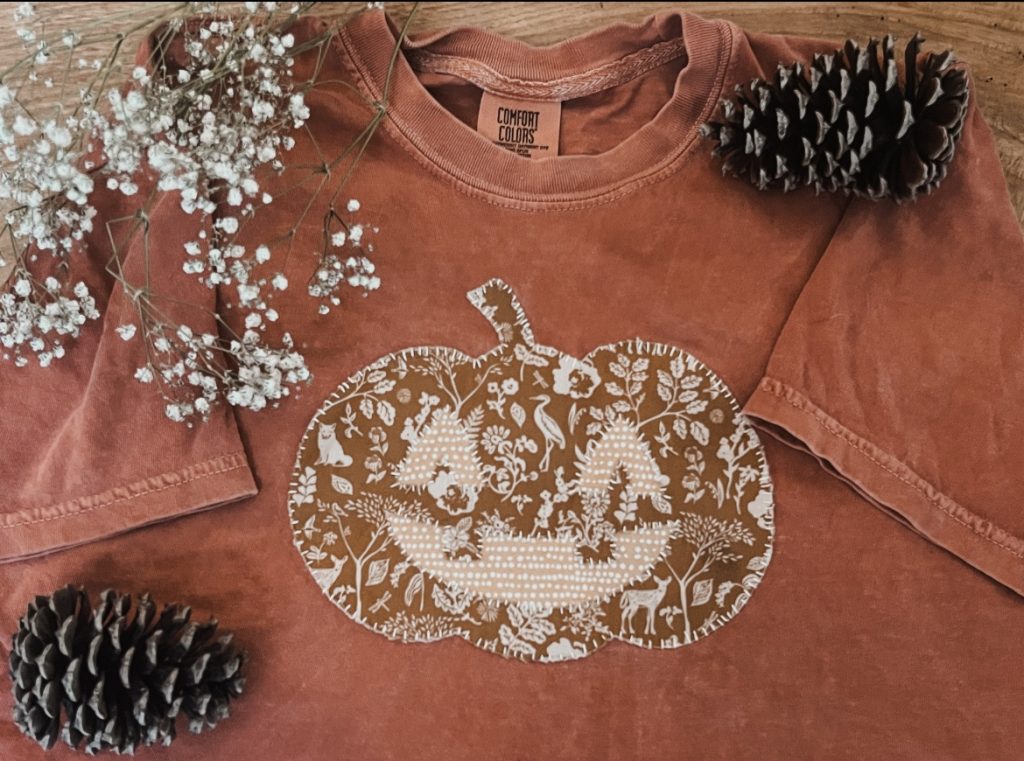 Rust colored t shirt with a floral pumpkin applique sewn on it
