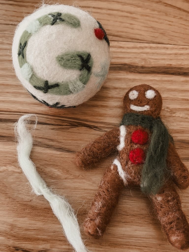Needle felted wool ball ornament and needle felted gingerbread man laying on a table top.
