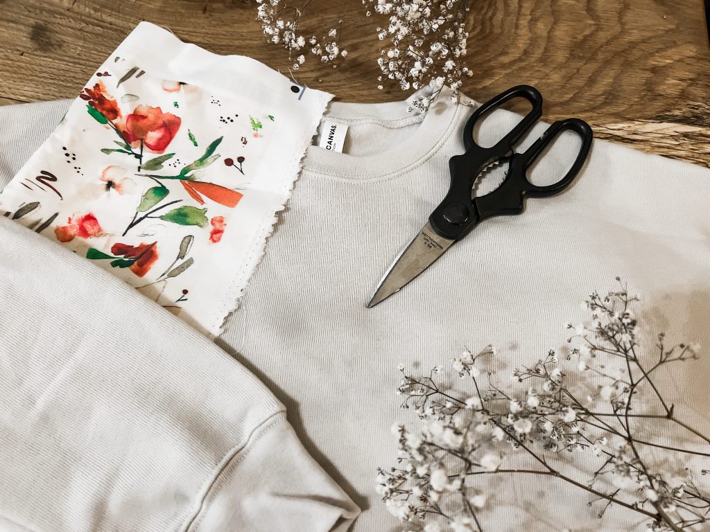 A blank grey sweatshirt laying on a table with pink floral fabric, scissors, and dried flowers. A Cricut fabric applique tutorial 
