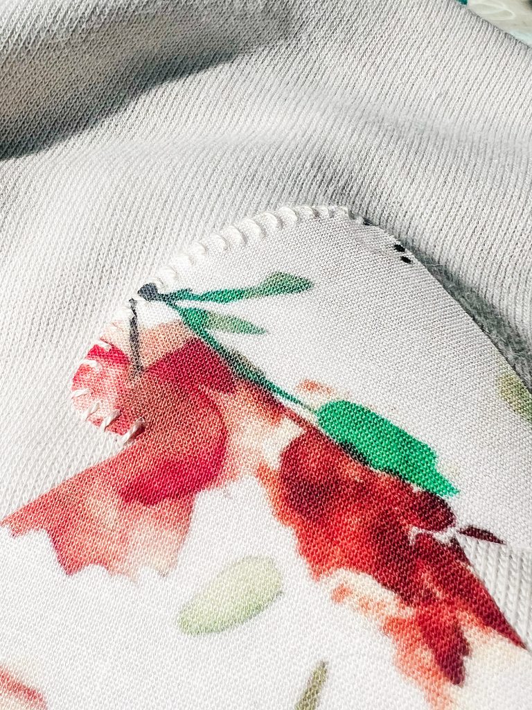 A close up of a fabric applique being sewn on a sweatshirt using a whip stitch .