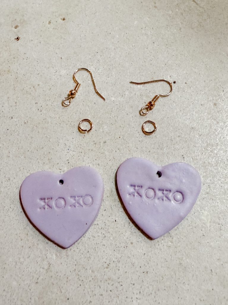 Stamped polymer clay heart earrings, earring hooks, and jump rings on a table. How to make polymer clay earrings for Valentine’s Day.