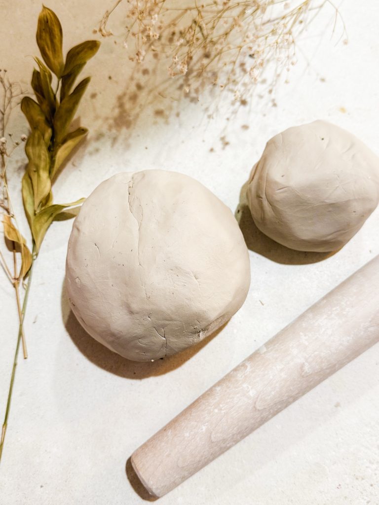 Balls of white stoneware clay, a wooden rolling pin, and dried flowers