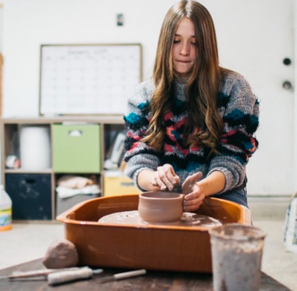 Woman throwing a pottery bowl at a pottery wheel in a white art studio