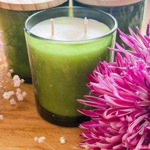 Nontoxic coconut soy wax candle in a green glass jar on a wood table with purple flowers