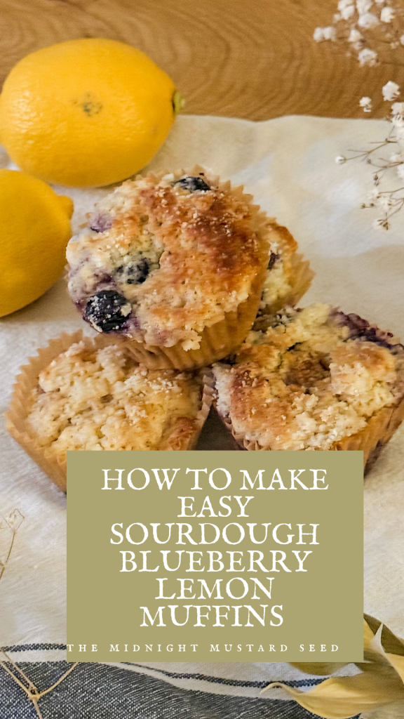 A picture of sourdough blueberry lemon muffins on a table with lemons and flowers. The text reads “How to make sourdough blueberry lemon muffins” by the midnight mustard seed
