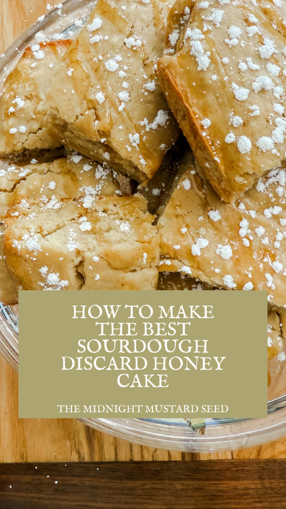 A close-up image of a tray filled with golden-brown sourdough discard honey cake slices, dusted with powdered sugar and drizzled with honey. The cake pieces are stacked and arranged in a clear glass dish placed on a wooden surface. A green text box overlays the bottom part of the image with the text “HOW TO MAKE THE BEST SOURDOUGH DISCARD HONEY CAKE” in white, and “THE MIDNIGHT MUSTARD SEED” in smaller white text below it.