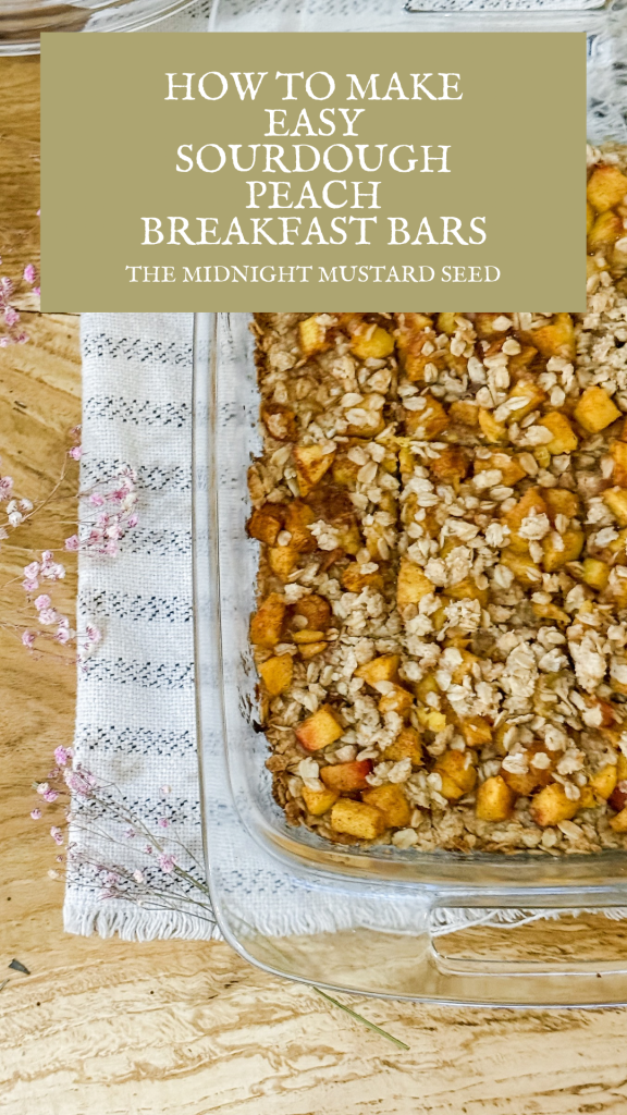 A baked sourdough peach breakfast bar with a golden oat topping and chunks of peach, served in a glass baking dish on a wooden table. The dish is placed on a striped cloth with pink dried flowers beside it. The blog title “The Midnight Mustard Seed” is visible at the top, along with the text “HOW TO MAKE EASY SOURDOUGH PEACH BREAKFAST BARS” in a green banner.